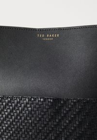 Malinha de couro preta com textura trançada na base, nome da marca gravado em dourado e design elegante e estruturado.
