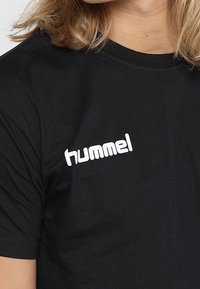Sort bomulds t-shirt med rund hals og korte ærmer. Udstyret med hvidt "hummel" logo på venstre brystområde. Blød tekstur.