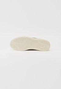 Semelle de sneaker noire avec une surface en caoutchouc beige texturé. Présente des motifs d'éléments hexagonaux et courbes pour l'adhérence.