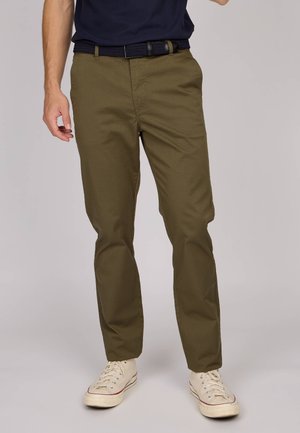 Pantalons vert olive en mélange de coton, avec une coupe droite, des passants de ceinture et des poches latérales, associés à des baskets en toile blanches.