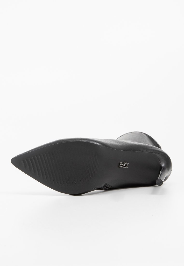 Czarny skórzany but na wysokim obcasie z orzechowym noskiem, gładką teksturą i szczegółowym metalowym akcentem na obcasie. Podeszwa z teksturą antypoślizgową.