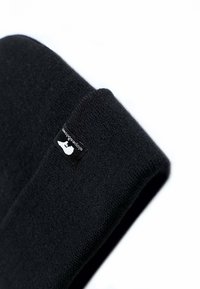 Berretto lavorato a maglia nero con una texture liscia e un risvolto. Presenta un'etichetta nera rettangolare con dettagli del logo bianco.