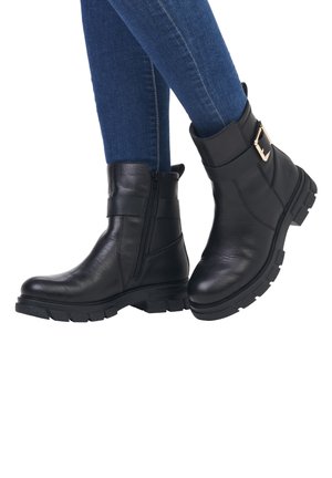 Schwarze Leder-Stiefeletten mit seitlichem Reißverschluss, dicker Gummisohle und einem dekorativen Riemen mit goldener Schnallendetail. Glatte Textur.