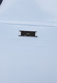 Hellblaues Sportmaterial mit einer glatten Textur, versehen mit einem schwarzen Metall-Logoakzent. Nahtloses Design mit subtilen Rippmustern.
