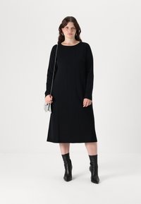 Abito lungo nero a maniche lunghe con scollatura tonda, caratterizzato da dettagli a cucitura verticale. Indossato con stivali neri con tacco e una borsa a tracolla argento.