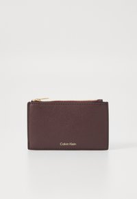 Burgundska kožna novčanik s teksturiranom površinom, zlatnim zatvaračem i urezanim logotipom "Calvin Klein" na prednjoj strani. Kompaktni pravokutni oblik.
