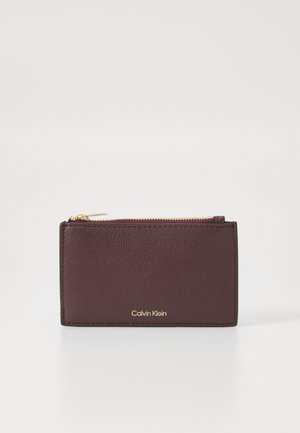 Burgundy leather wallet with a textured surface, gold zipper closure, and embossed "Calvin Klein" logo on the front. Compact rectangular shape.