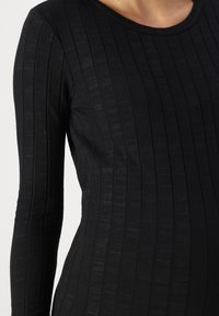 Μαύρο μακρυμάνικο τοπ από ραμμένο ύφασμα, με κάθετες υφασμένες ρίγες και στρογγυλή λαιμόκοψη. Κατάλληλο για καθημερινές εμφανίσεις.