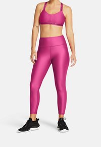 Reggiseno sportivo rosa con logo nero, abbinato a leggings rosa coordinati. Entrambi i capi presentano un tessuto morbido e elasticizzato. Scarpe da ginnastica nere completano l'outfit.