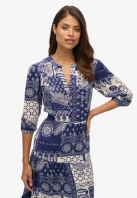 Blau- und cremefarbenes gemustertes Kleid mit drei Viertelärmel, Knopfleiste und gestuftem Rock. Verziert mit Paisley- und Blumenmustern.