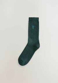 Dunkelgrüner, gerippter Socke mit verstärktem Zehenbereich, ausgestattet mit einer kleinen blauen Logo-Stickerei in der Nähe des Bündchens. Hergestellt aus weichem, strukturiertem Material.