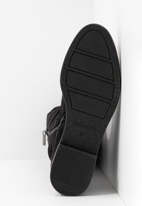 Stivale alla caviglia in suede nero con suola in gomma texturizzata, dotato di una cerniera laterale e un design superiore liscio.