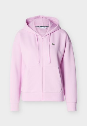 Sweat à capuche zippé rose clair avec cordons de serrage, poches kangourou, poignets côtelés et petit logo crocodile vert sur la poitrine.