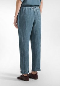 Lichtblauwe, losvallende linnen broek met een elastische tailleband, omgeslagen zomen en een achterzak. Gecombineerd met donker bordeauxrode lage schoenen.