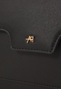 Portafoglio in pelle nera testurizzata con logo metallico dorato, dettagli di cucitura sottili e chiusura a patta per un accesso sicuro.