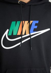 Il felpa nera presenta un notevole logo "NIKE" multicolore con accenti verdi, arancioni, blu e bianchi, e un cappuccio con il cordino.