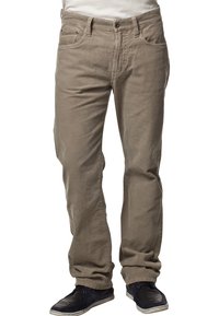 Jasnobrązowe spodnie sztruksowe o prostym kroju, z zamkiem błyskawicznym, pięcioma kieszeniami i subtelną fakturą prążków. Noszone z ciemnymi butami.