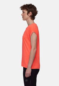 Kortärmad T-shirt med rund halsringning i klar korall, tillverkad av mjukt tyg med rullade ärmar. Tryckt design på framsidan. Svarta byxor synliga.