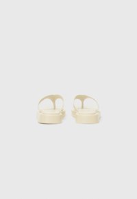 Infradito beige con finitura liscia e opaca, caratterizzate da un design minimalista e due cinturini arrotondati sopra una base piatta.