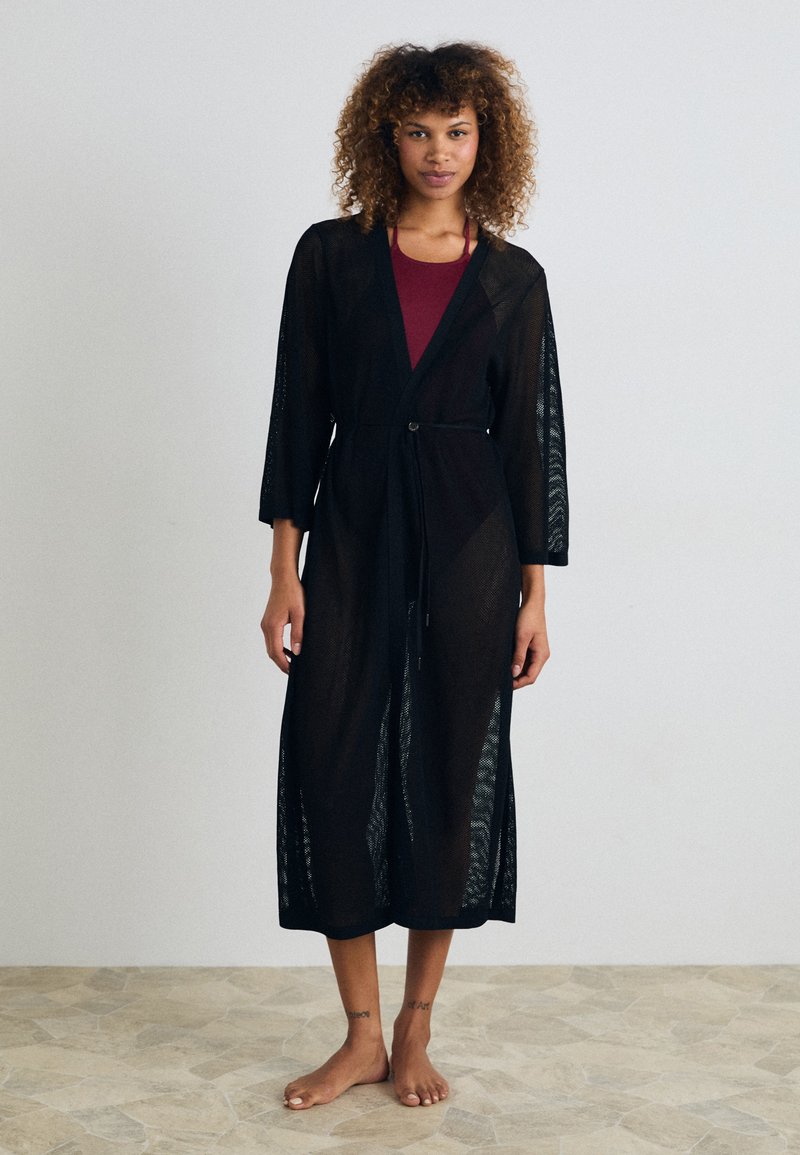 Mustmust muströöp, avatud ees, kolmveerandvarrukatega ja paeltega. Muströöp on laia lõikega ja pikk.