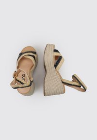 Wedges de esparto beige con tiras elásticas a rayas negras, plataforma de yute trenzado y plantilla de cuero suave. Parte trasera cerrada con hebilla ajustable.