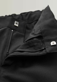 Tissu noir avec une surface texturée, doté d'une poche zippée et d'accents métalliques. Le tissu possède une doublure lisse et des coutures renforcées.