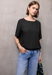 Top nero a maniche corte realizzato in tessuto leggero, abbinato a jeans di denim blu chiaro. L'outfit presenta una vestibilità comoda e una texture liscia.