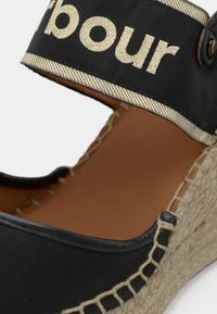 Espadrille noire avec une tige en toile texturée, dotée d'une sangle beige avec texte imprimé, et une semelle enveloppée de jute pour un détail supplémentaire.