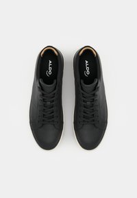 Svarte lærersneakers med teksturert overflate, flate lisser og lys gummisåle. "ALDO"-logo synlig på innersålen.