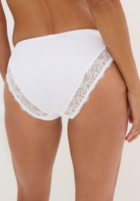 Culotte en coton blanc avec des accents en dentelle sur les bords. La dentelle présente un design festonné avec un motif floral et une finition lisse.