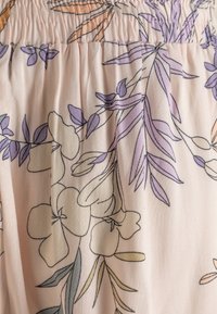Bloemige stofstaal in zachtroze, met paarse en gele contouren van bladeren en bloemen, met geplooide textuur aan de bovenkant.