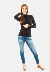 Zwarte geribbelde top met lange mouwen, een hoge kraag en gegolfde manchetten, gecombineerd met lichtblauwe slim fit jeans en beige sneakers met rode accenten.