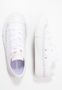 Baskets en toile blanche à bout rond, avec des coutures en zigzag multicolores le long des côtés et des semelles en caoutchouc blanches.