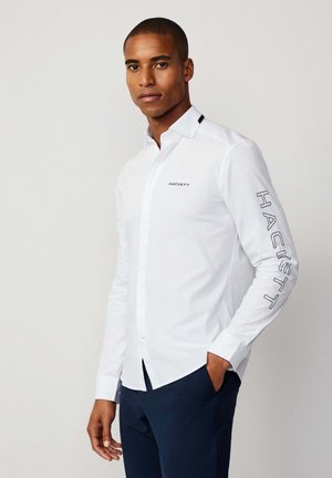 Weißes Langarmhemd mit Button-Down-Kragen, mit dem Logo "HACKETT" auf der Brust und dem Ärmel in Marineblau. Glattes Material, taillierte Passform.