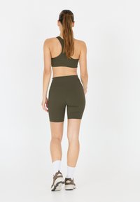 Olijfgroen sportoutfit met een mouwloos crop top en shorts tot halverwege de dij, gemaakt van rekbaar materiaal met een gladde textuur.