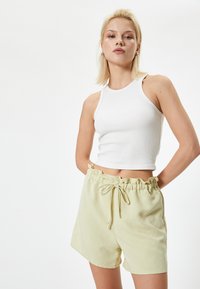 Hvid ribbet crop tank top parret med lysegule shorts med snor i taljen, der har en volangkant og blødt, svævende stof.