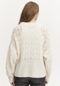 Weißer Strickpullover mit strukturiertem Muster, geripptem Saum und weitem Ärmel. Hergestellt aus weichem Material und mit offenen Maschen durchzogen.