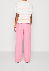 Camiseta de manga corta a rayas en blanco, con colores pastel; combinada con pantalones rosas holgados que presentan un diseño limpio y a medida.