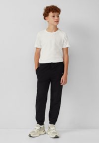 Witte T-shirt met korte mouwen en ronde hals, gecombineerd met zwarte joggerbroek met elastische boorden en zijzakken. Grijze sportschoenen maken de look af.