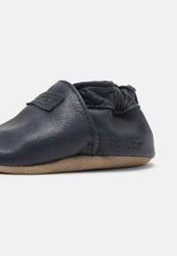 Scarpina per neonati in pelle blu navy con suola morbida, parte superiore elasticizzata e superficie testurizzata. Presenta un piccolo logo sul lato.