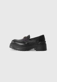 Black leather loafer with chunky textured sole and a gold buckle detail on the top, set against a plain light background.