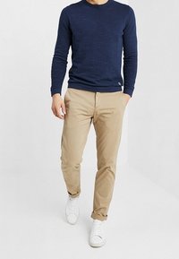 Marineblauwe geribde lange mouwen crewneck trui gecombineerd met beige chino's en witte sneakers, wat een casual outfit toont die geschikt is voor dagelijks gebruik.