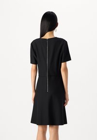 Vestido preto de manga curta com corpete ajustado e saia rodada. Apresenta um fecho éclair nas costas visível e um tecido liso e estruturado.