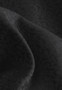 Schwarzer Stoff mit einem dezente Ton-in-Ton-Leopardenmuster, einer glatten Textur und einem sanften Fall, der Tiefe in das Material bringt.