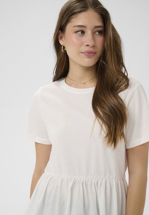 Junge Frau mit langen braunen Haaren, die goldene Creolen, eine zarte goldene Halskette und ein weißes Kurzarmkleid trägt und seitlich schaut.