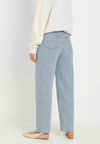 Jeans azzurri a vita alta con una vestibilità dritta, dotati di tasche posteriori e un leggero effetto sbiadito, abbinati a scarpe basse chiare.