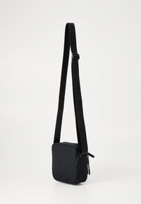 Sort crossbody taske med firkantet form, tekstureret stof, lynlåslukning og justerbar rem med mærkenavnet iøjnefaldende.