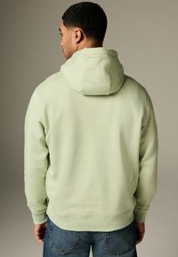 Light green hoodie with a relaxed fit, soft texture, and a rounded hood. Features ribbed cuffs and waistband, worn with blue jeans.