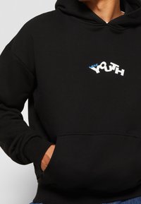 Felpa nera con cappuccio e tasca frontale, caratterizzata da un design grafico testuale in bianco e blu con la scritta "YOUTH" sul petto. Tessuto morbido, vestibilità comoda.