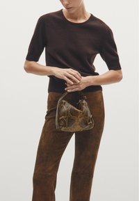 Brown knitted short-sleeve sweater worn with brown suede pants. The model holds a textured brown and gold snake-print handbag.